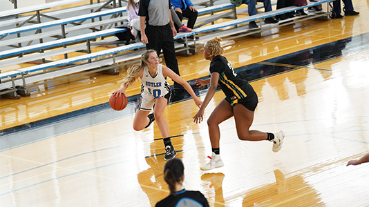 Women's basketball player dribbles ball away from opponent.