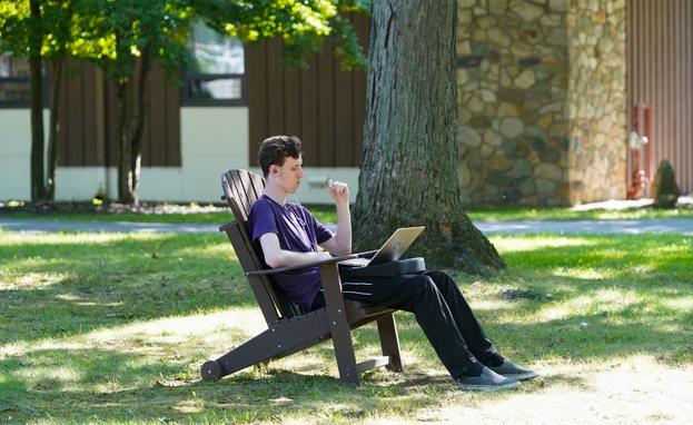 Student on laptop sitting in oak grove